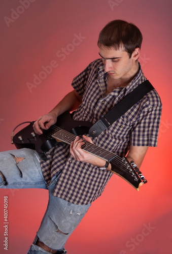 Expressive young man playing guitar on red background. Musician in beautiful hall. 