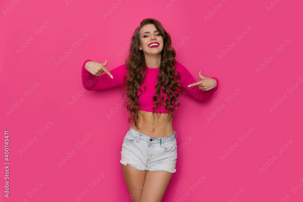 Happy Young Woman In A Short Pink Sweater Is Pointing To Her Waist Happy Young Woman In A Short Pink Sweater Is Pointing To Her Waist