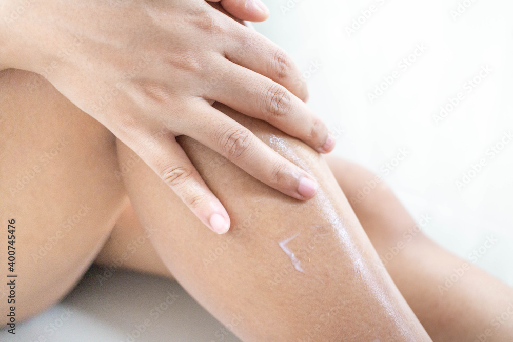Fototapeta premium The woman sitting on the ground Use your hands to apply the cream on your legs.