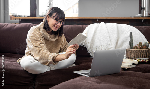 Young cheerful woman in glasses with a book in her hands behind a laptop at home on the couch. © puhimec