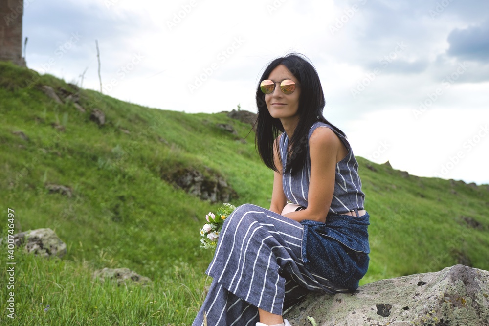 Young brunette caucasian woman sit on the rock and hold flower bouquet in hand and smile Young brunette caucasian woman sit on the rock and hold flower bouquet in hand and smile