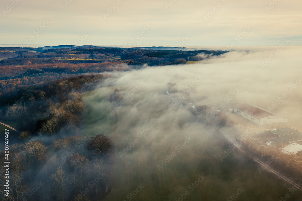 Aerial view of rural landscape and farm in the winter fog, moody atmosphere
