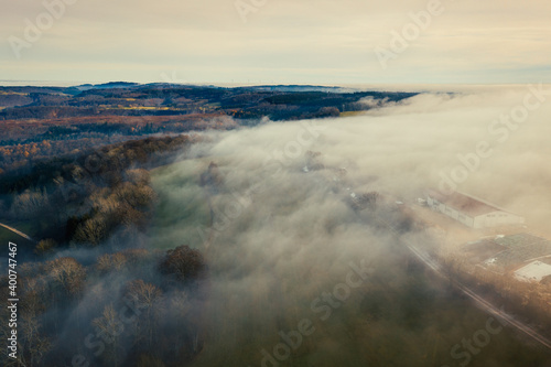 Aerial view of rural landscape and farm in the winter fog, moody atmosphere 