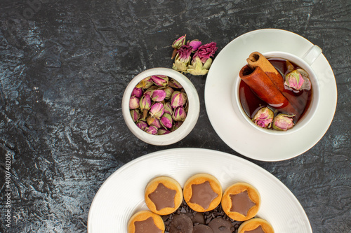 a cup of herbal tea with half view of cookie on white plate and a bowl of dry flower on grey geound photo