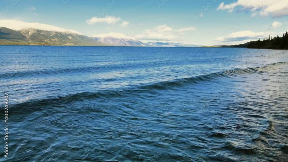 Small waves washing over Atlin Lake shore. White mountain peaks on background. Small waves washing over Atlin Lake shore. White mountain peaks on background.