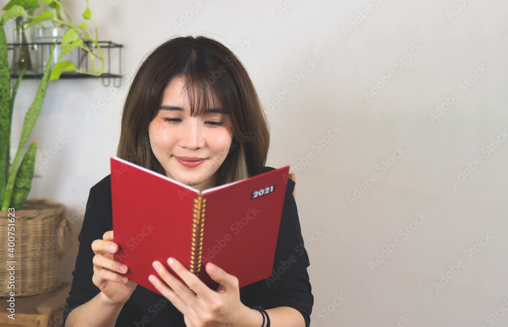 Asian woman open red 2021 diary, smiling . white wall with house plant background. Asian woman open red 2021 diary, smiling . white wall with house plant background.