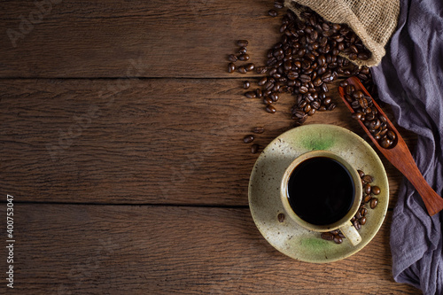 Top view above of Black hot fresh coffee in brown ceramic cup with coffee beans roasted in burlap sack bag on wooden table background. Flat lay with copy space.