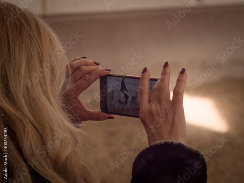 Blonde female making video with phone at dressage contest.
