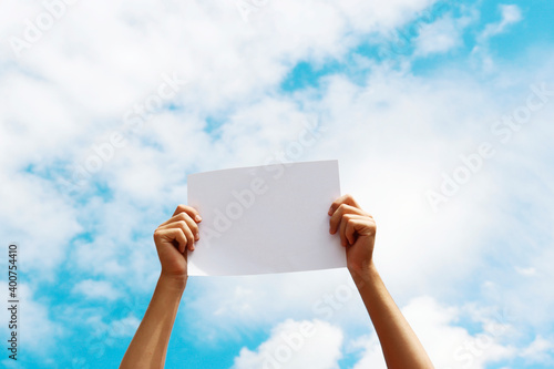 a blank sheet of paper in the hands of a young guy against a blue sky with clouds