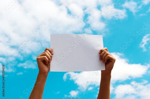 a blank sheet of paper in the hands of a young guy against a blue sky with clouds