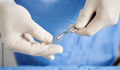 Close up view of doctor's hands getting ready scalpel for plastic surgery. Surgeon with stainless steel medical instrument in arms wearing white sterile gloves. Concept of surgery and medicine.