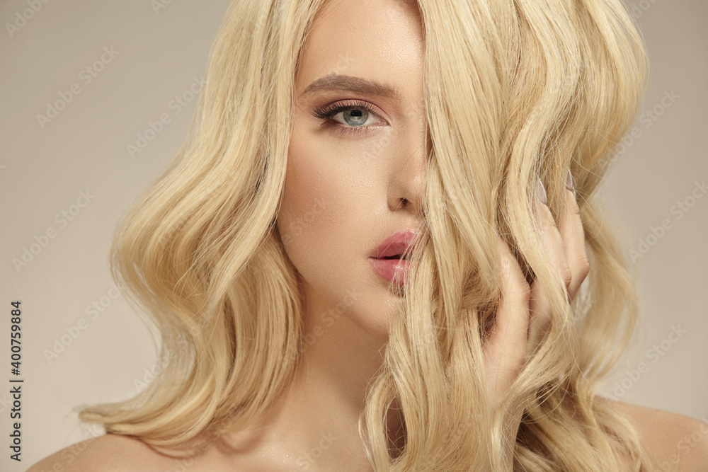 Female beauty, hairstyle of blonde long wavy hair. Caucasian attractive woman has a natural curly hairstyle, close up shot on a beige isolated. Female beauty, hairstyle of blonde long wavy hair. Caucasian attractive woman has a natural curly hairstyle, close up shot on a beige isolated.