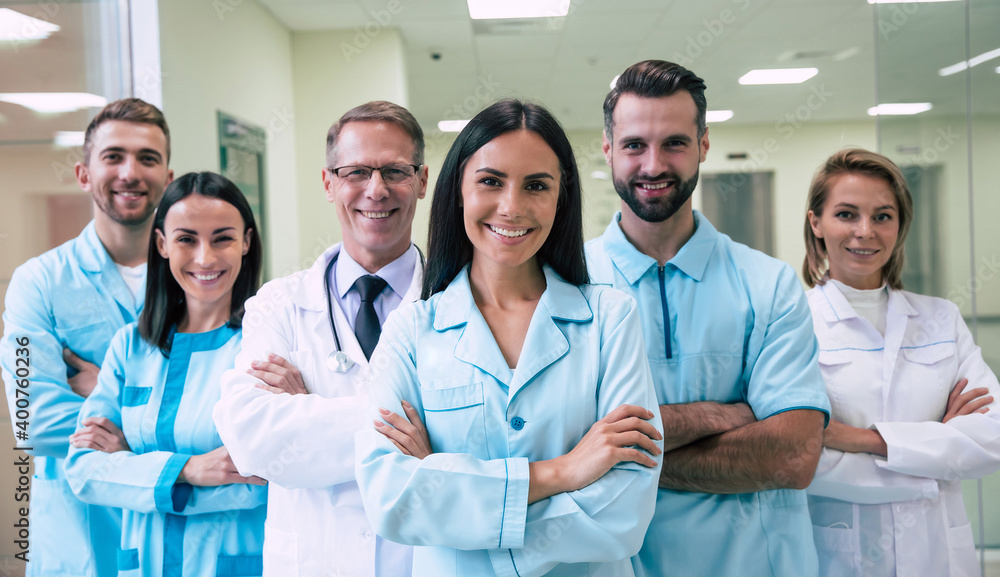 Happy team of successful and confident modern medical doctors are posing and looking on the camera at the hospital corridor