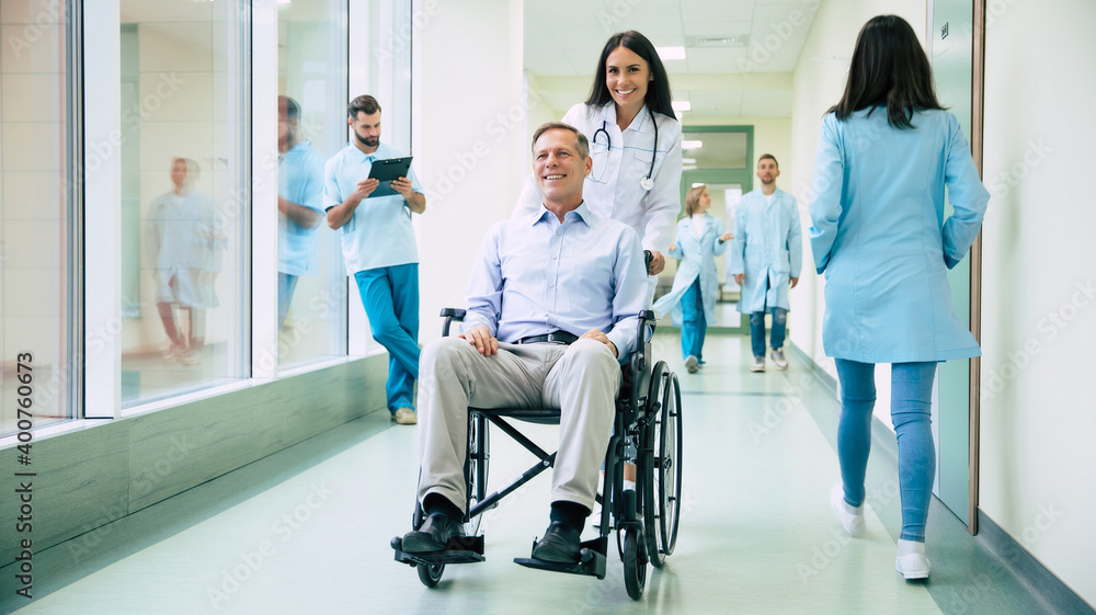 Obraz premium Senior handsome man in a wheelchair is moving in the hospital with help of medical special staff