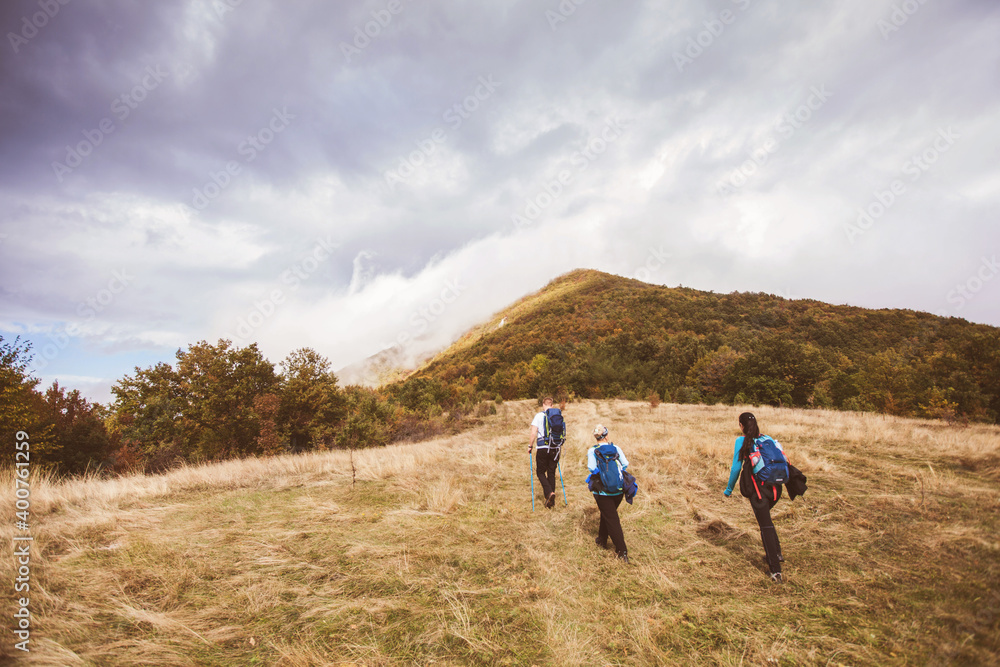 Group of active people hiking on autumn day through beautiful nature landscape. Misty Mountain Peak. Rear View. Cloudy sky in the background.