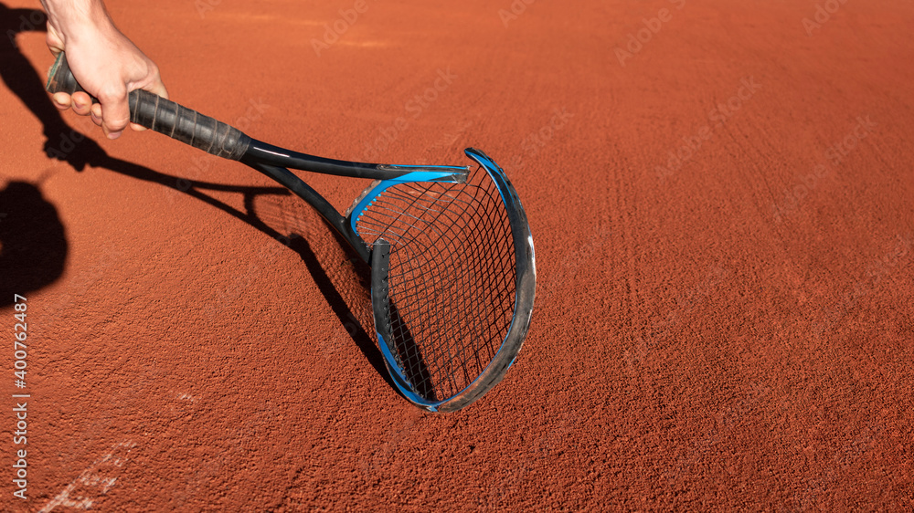 Frustrated tennis player broke his racket in fit of anger. Broken tennis racket on clay tennis court. Mental health in sports. Negative emotions, stress, dissatisfaction, defeat, crash, failure, loss