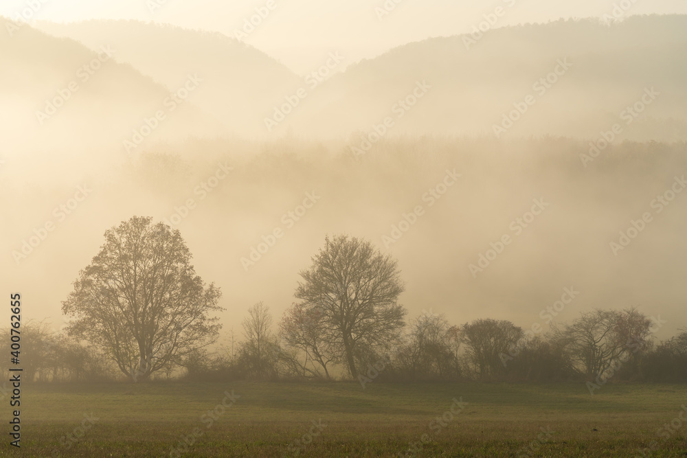 Scenic view of thick fog rolling over valley at sunrise. Beautiful autumnal landscape background