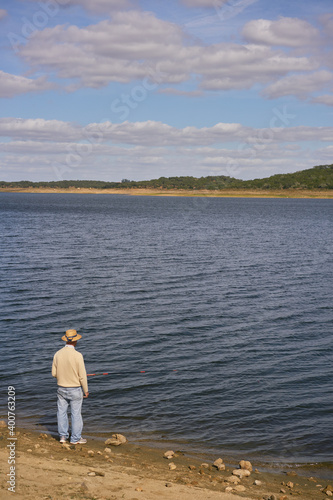 Caucasian senior man fishing with a straw hat on a dam lake reservoir in Alentejo, Portugal