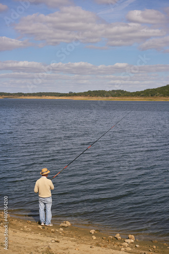 Caucasian senior man fishing with a straw hat on a dam lake reservoir in Alentejo, Portugal