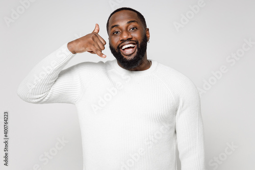 Excited cheerful young african american man 20s wearing casual basic sweater standing doing phone gesture like says call me back looking camera isolated on white color wall background studio portrait.