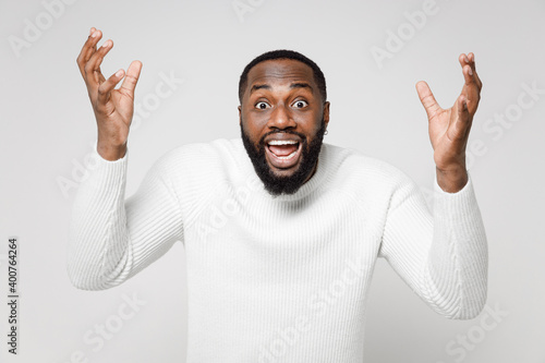 Shocked excited young african american man 20s wearing casual basic sweater standing keeping mouth open screaming spreading hands looking camera isolated on white color background studio portrait.