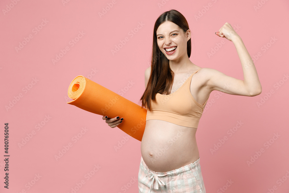 Young strong sporty fitness pregnant woman keeping hands on big belly stomach tummy with baby hold yoga mat isolated on pastel pink background studio. Maternity family pregnancy expectation concept Young strong sporty fitness pregnant woman keeping hands on big belly stomach tummy with baby hold yoga mat isolated on pastel pink background studio. Maternity family pregnancy expectation concept