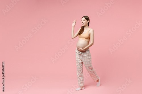 Full body length young pregnant woman in basic top stroking keeping hands on big belly stomach tummy with baby isolated on pastel pink background studio Maternity family pregnancy expectation concept