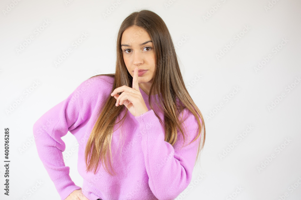 Portrait of peaceful beautiful girl in pink sweater looks directly in camera and showing silence gesture isolated over white background Portrait of peaceful beautiful girl in pink sweater looks directly in camera and showing silence gesture isolated over white background