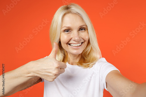 Wallpaper Mural Close up of cheerful elderly gray-haired blonde woman lady 40s 50s years old in white casual t-shirt doing selfie shot on mobile phone showing thumb up isolated on orange background studio portrait. Torontodigital.ca