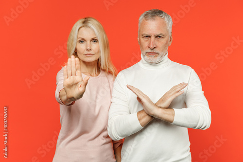 Displeased couple two friends elderly gray-haired man blonde woman in white pink casual clothes showing stop gesture with palm crossed hands isolated on bright orange wall background studio portrait.