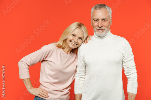 Smiling cheerful funny couple two friends elderly gray-haired man blonde woman wearing white pink casual clothes standing looking camera isolated on bright orange color background studio portrait. © ViDi Studio