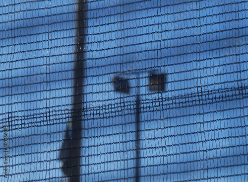 blurred streetlight behind the net of a playing field with clear blue sky
