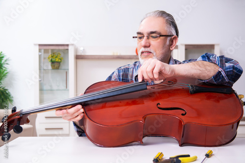 Obraz na plátně Senior male repairman repairing musical instruments at home