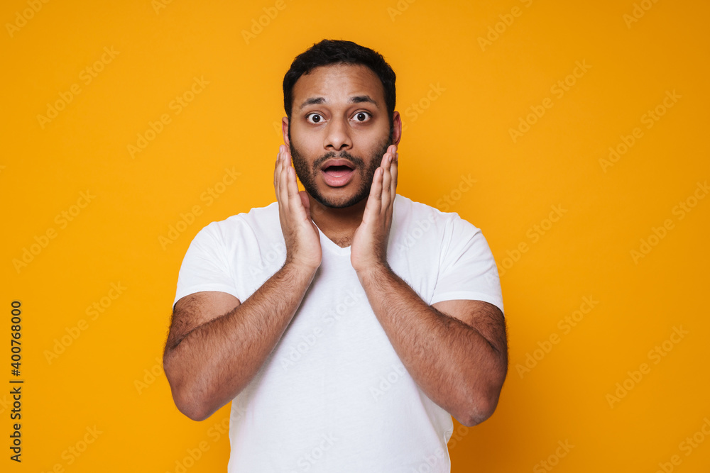 Asian brunette unshaven surprised man raising hands to his face Asian brunette unshaven surprised man raising hands to his face
