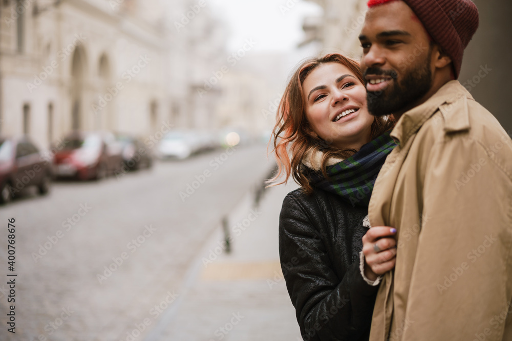 Multinational couple hugging and laughing while walking on city street Multinational couple hugging and laughing while walking on city street
