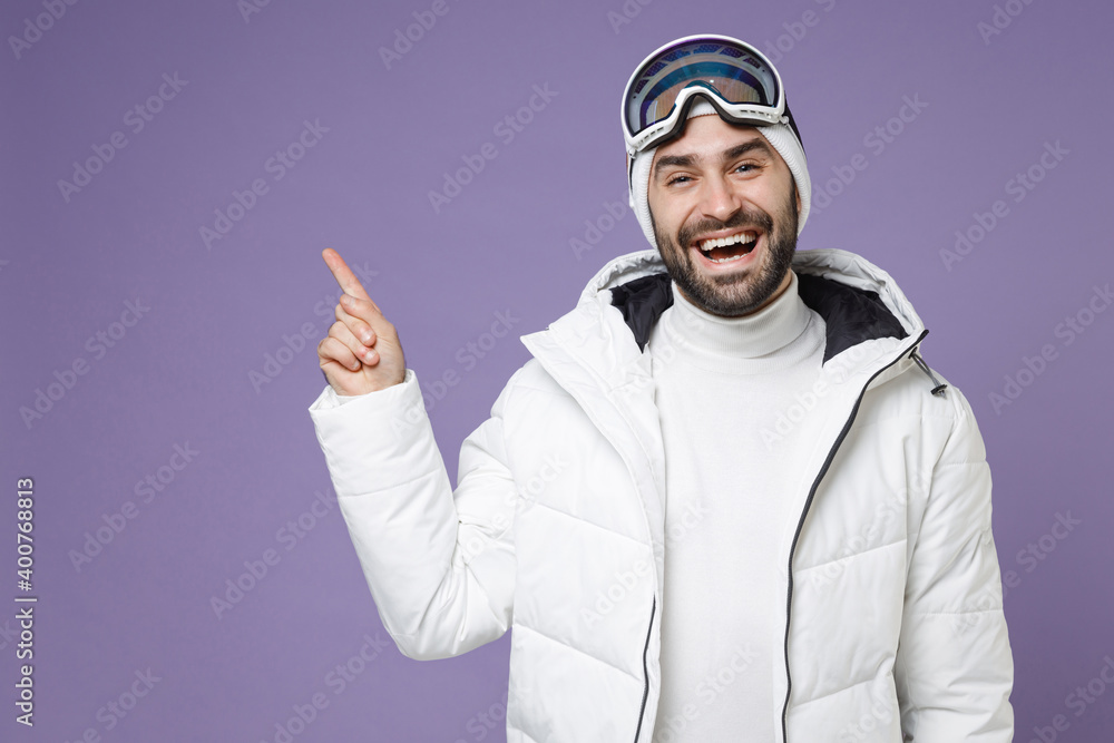 Cheerful skier man in white windbreaker jacket ski goggles mask pointing index finger up spend extreme weekend winter season in mountains isolated on purple background. People lifestyle hobby concept. Cheerful skier man in white windbreaker jacket ski goggles mask pointing index finger up spend extreme weekend winter season in mountains isolated on purple background. People lifestyle hobby concept.