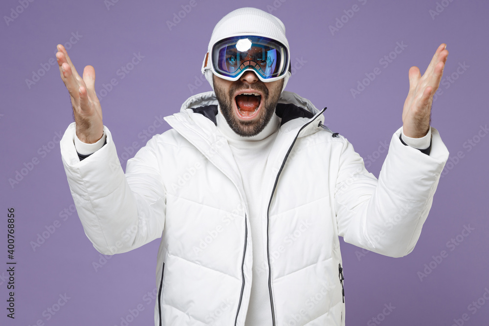 Angry skier man in white windbreaker jacket ski goggles mask spreading hands swearing spend extreme weekend winter season in mountains isolated on purple background. People lifestyle hobby concept. Angry skier man in white windbreaker jacket ski goggles mask spreading hands swearing spend extreme weekend winter season in mountains isolated on purple background. People lifestyle hobby concept.