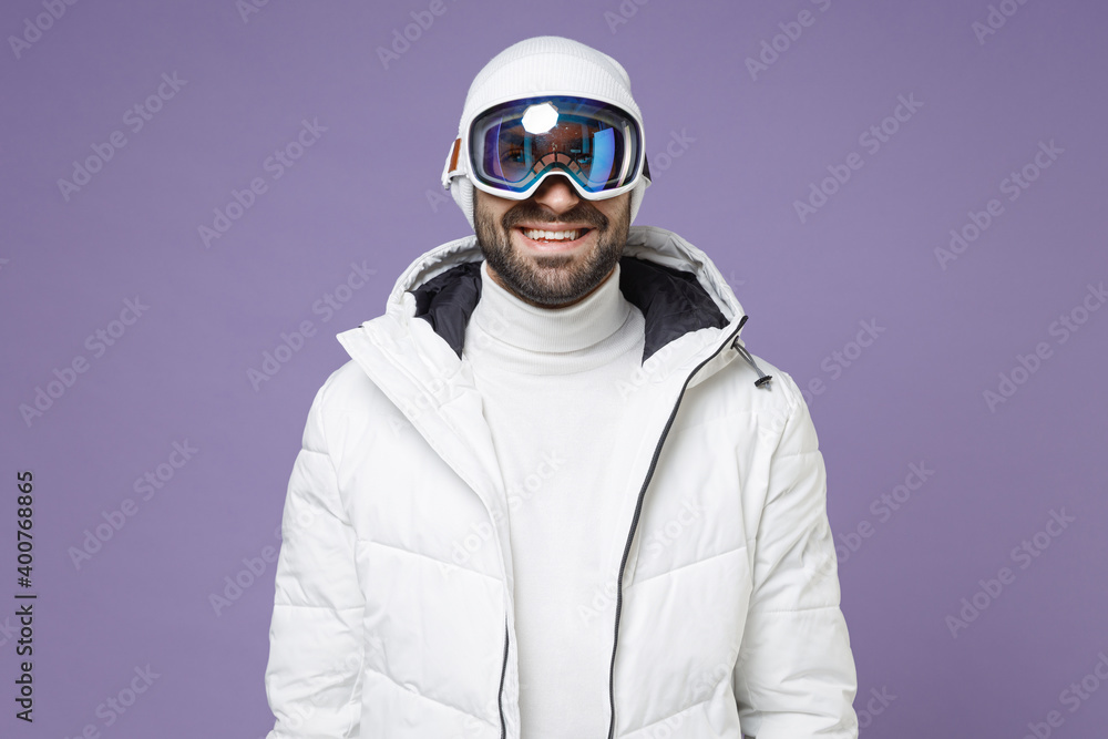 Smiling skier man in warm white padded windbreaker jacket ski goggles mask going to spend extreme weekend winter season in mountains isolated on purple background. People lifestyle hobby concept. Smiling skier man in warm white padded windbreaker jacket ski goggles mask going to spend extreme weekend winter season in mountains isolated on purple background. People lifestyle hobby concept.