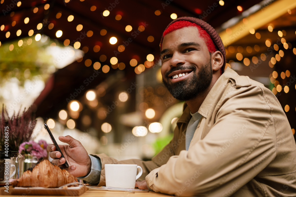 Young african american happy man using cellphone in cafe outdoors Young african american happy man using cellphone in cafe outdoors