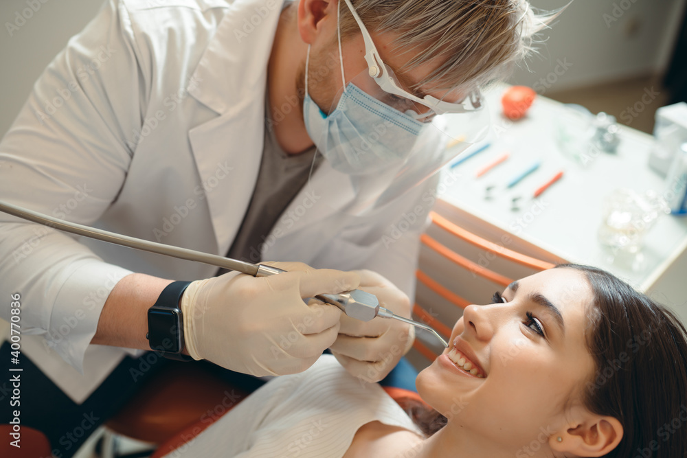 Fototapeta premium Dental doctor in protective glasses examines the mouth of a smiling girl