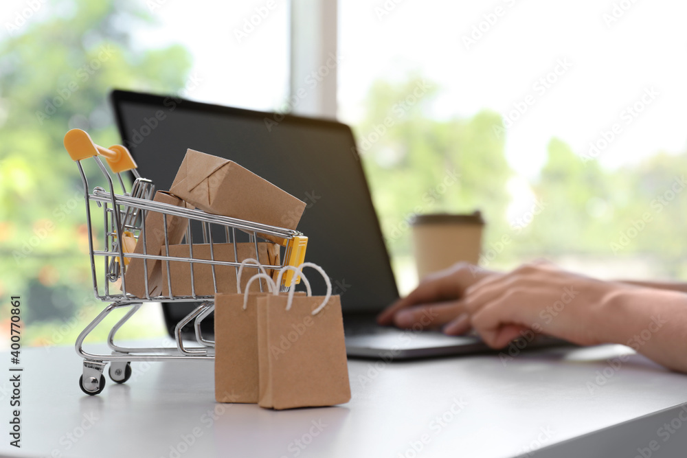 Internet shopping. Small cart with boxes and bags near woman using laptop indoors Internet shopping. Small cart with boxes and bags near woman using laptop indoors