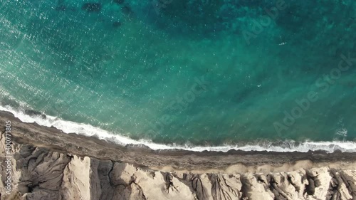 Top-down aerial view of turquoise blue ocean waves breaking on the shore of pristine tropical sand beach Santorini