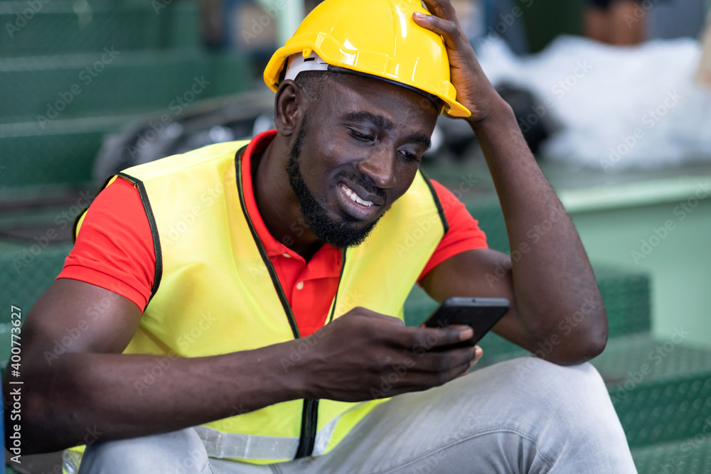 Engineer man wearing a safety helmet, vest sitting in the automotive parts warehouse factory. Industrial worker Looking at smartphone and smile. Finding information from the phone. Knowledge concept
