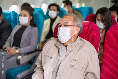 Asian passengers wearing medical face mask sitting on seat in the airplane cabin. travel on holiday, vacation or work abroad during Coronavirus epidemic. new normal lifestyle and social distancing