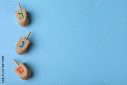 Hanukkah traditional dreidels with letters He, Pe and Nun on light blue background, flat lay. Space for text photo