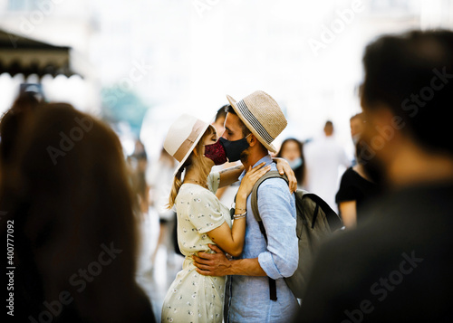 Couple in love covered by facemask kissing in the city - New normal lifestyle concept with boyfriend and girlfriend walking in the street wearing medial mask photo