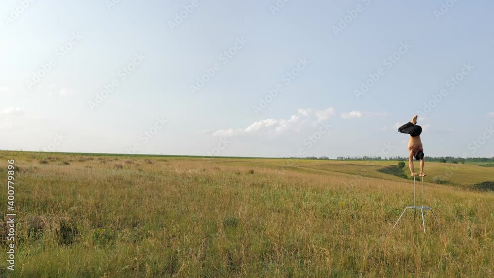 A man of athletic build performs complex gymnastic exercises in a field at sunset A man of athletic build performs complex gymnastic exercises in a field at sunset