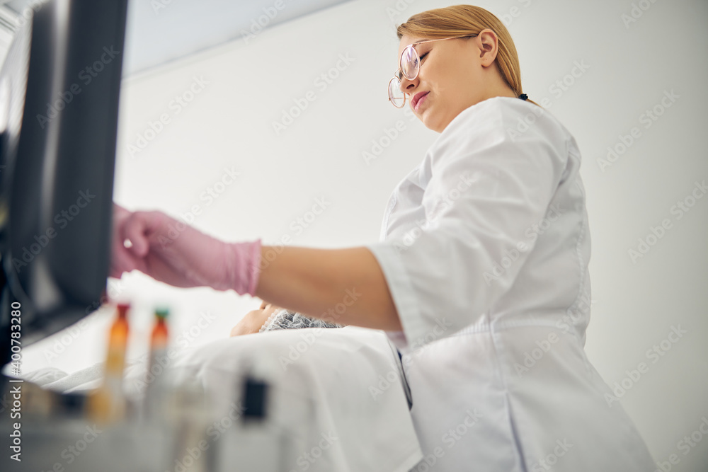 Beautician in eyeglasses starting a cosmetic procedure Beautician in eyeglasses starting a cosmetic procedure