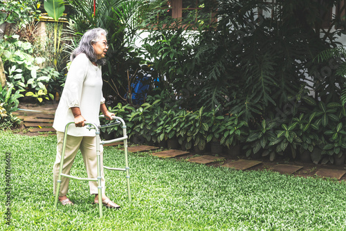 Elderly woman in the walk with a device such as cane walker to support the walk on green lawn, to retirement age and health care concept.