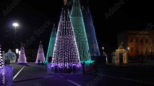 Evening Russia, Samara, Kuibyshev Square, New Year trees completely decorated with bulbs glow with different patterns and people walk photo